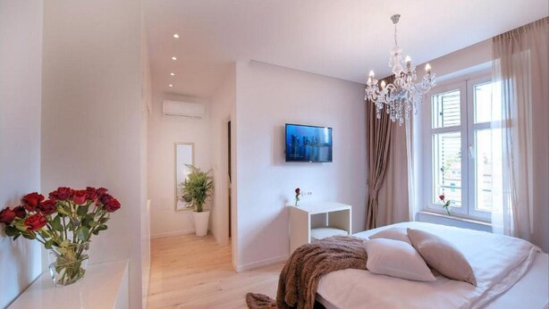 A bedroom with a bed, a TV, a chandelier, and a window with curtains. - Via Porto Rooms - Deluxe Room with King Bed (Split)