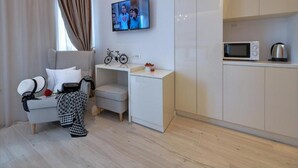 A modern hotel room with a seating area, a television mounted on the wall, a microwave, and a kettle on the countertop. - Via Porto Rooms - Deluxe Double Room with Double Bed and Balcony (Split)