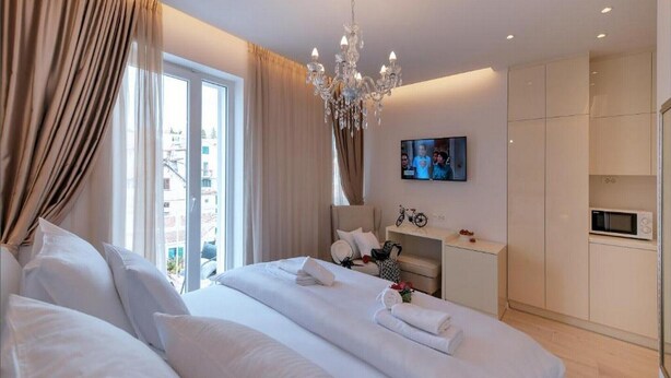 A modern hotel room with a large bed, a television, a minibar, and a view of the city. - Via Porto Rooms - Deluxe Double Room with Double Bed and Balcony (Split)