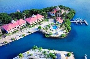 Vista aérea de un complejo turístico con varias edificaciones, una piscina y un muelle con barcos.