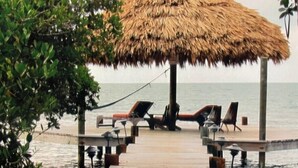 Un muelle de madera que conduce a una estructura con techo de paja y sillas de descanso.