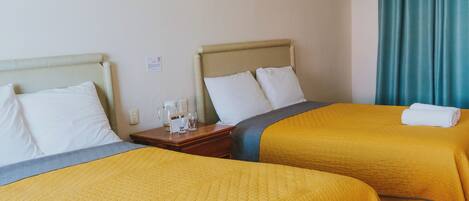 Habitación de hotel con dos camas, cada una con cubrecama amarillo, un cuadro en la pared y una ventana con cortinas color turquesa.