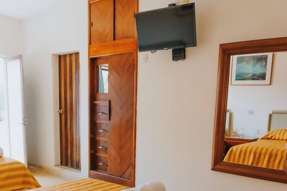 A hotel room with two beds, a wooden wardrobe, a television mounted on the wall, and a mirror reflecting the room.