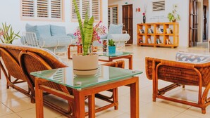 Um espaço amplo e interno com móveis de vime, uma mesa de vidro e plantas penduradas.