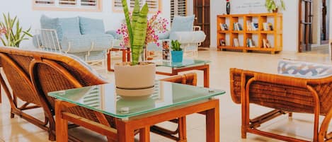 A spacious indoor area with wicker furniture, a glass table, and hanging plants.