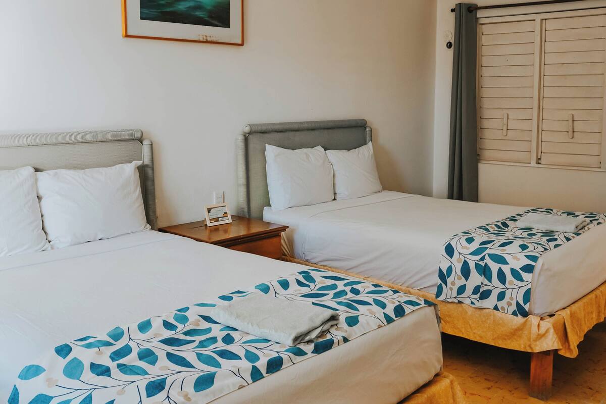 A hotel room with two beds, a framed picture on the wall, a wardrobe, and a tiled floor.