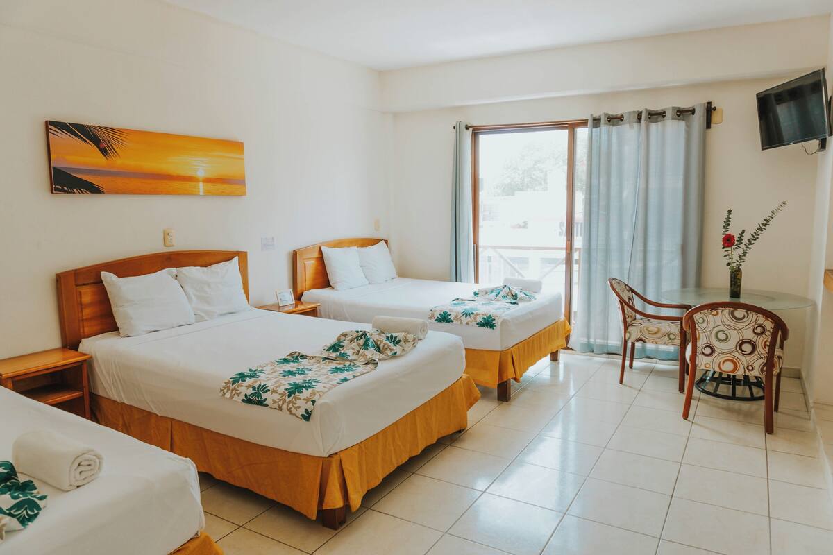 A hotel room with two beds, a TV, a dining table with chairs, and a painting on the wall.