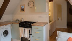 A compact kitchen with a washing machine, a stove, and a clock on the wall. - Countryside Loft in the heart of Bridgnorth (Bridgnorth)