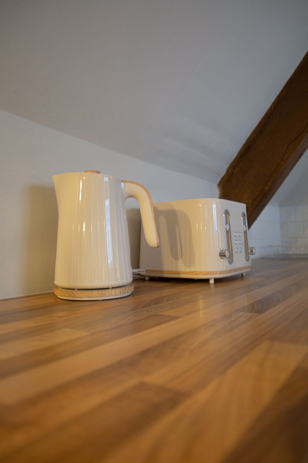 Twee witte keramieken koffiepotten op een houten vloer, voor een witte muur met een houten balk.