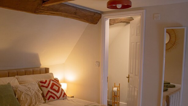 A bedroom with a wooden ceiling, a bed with a white mattress and green pillows, a bedside lamp, and a mirror on the wall. - Countryside Loft in the heart of Bridgnorth (Bridgnorth)