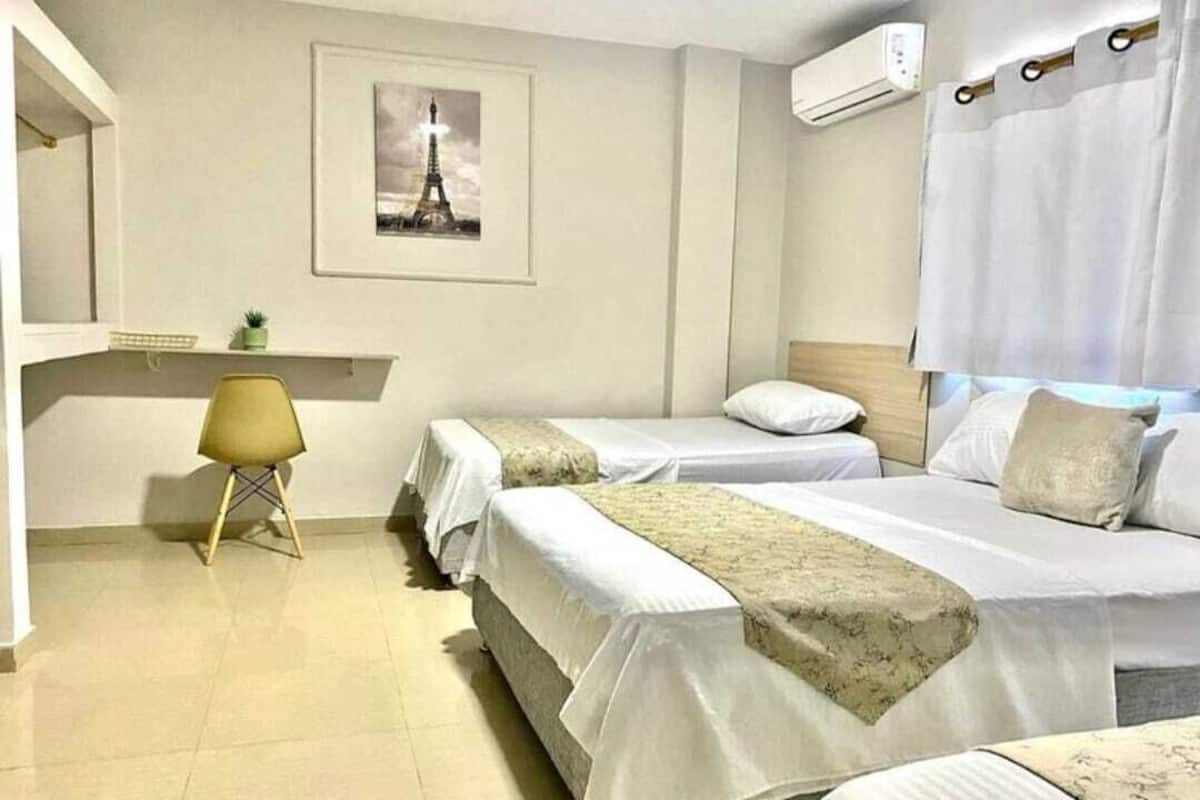 A hotel room with two beds, a chair, a picture of the Eiffel Tower, and a window with curtains.