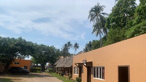 A row of thatched-roof cottages with a dirt path in between, surrounded by greenery and palm trees. - Hotel Fragatta playa el cuco  (El Cuco)