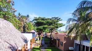 A pathway leading through a courtyard with thatched-roof structures, palm trees, and a stone pathway. - Hotel Fragatta playa el cuco  (El Cuco)