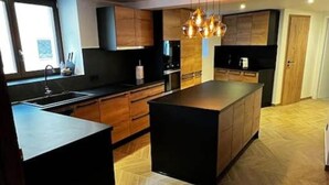 A modern kitchen with a large island, wooden cabinetry, and a herringbone floor pattern. - The Cottage (Guémar)