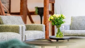 A modern living room with a round glass coffee table, a vase with yellow flowers, and grey upholstered sofas. - The Cottage (Guémar)