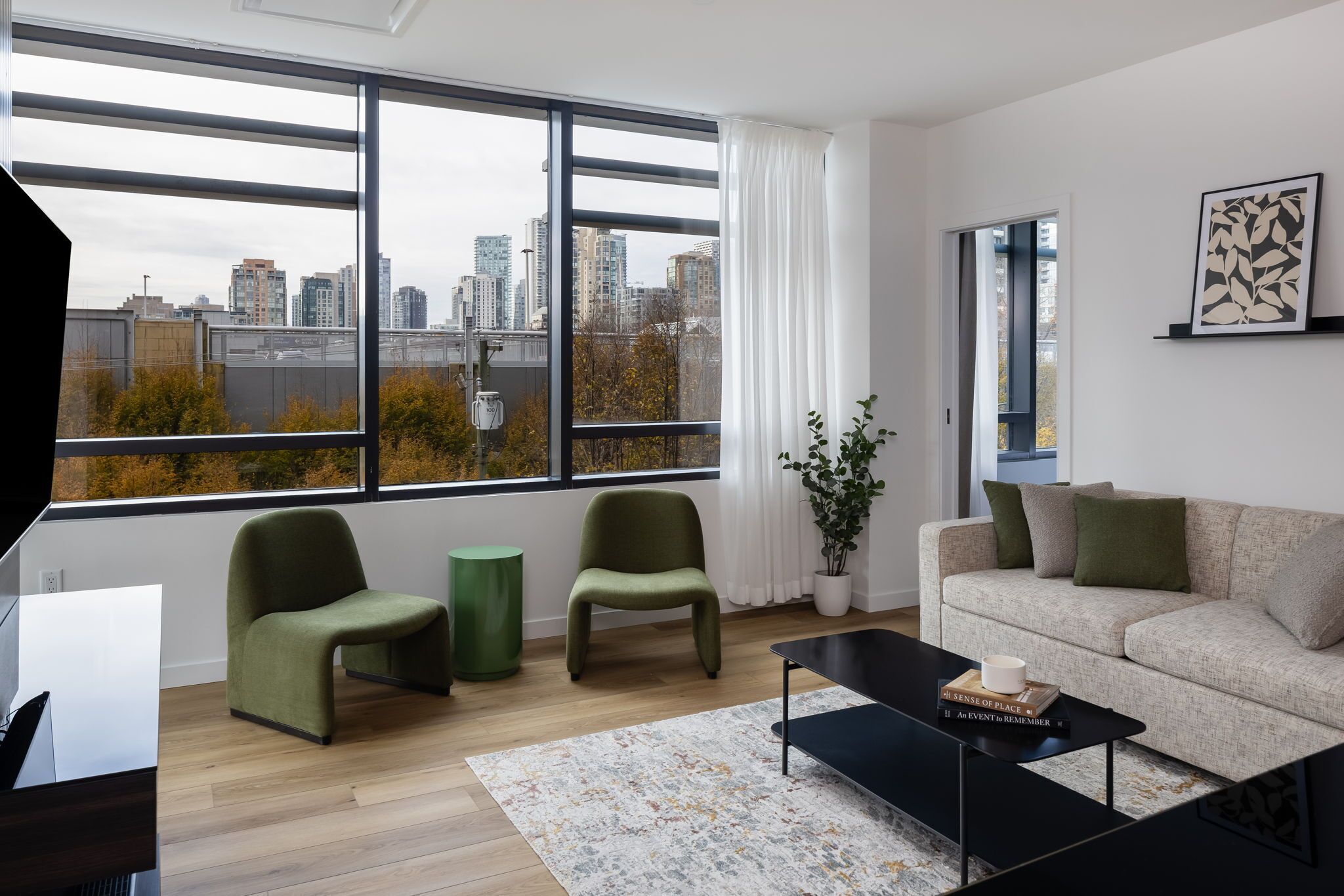 A modern living room with a large window, a sofa, two chairs, a coffee table, and a potted plant.
