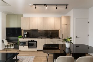 A modern kitchen with wooden cabinets, a black countertop, and a built-in oven. There is a dining area with a glass table and chairs.