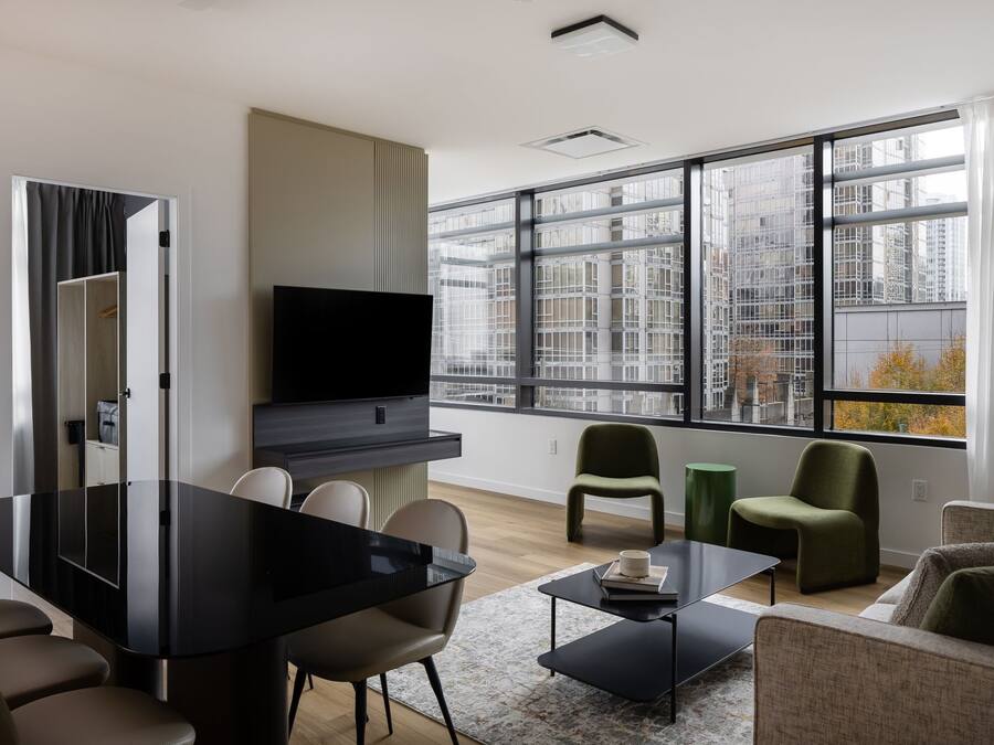 A modern living room with a dining area, large windows, and a flat-screen TV.