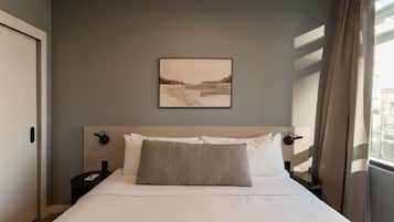 A hotel room with a bed, a nightstand, a wall-mounted lamp, and a window with curtains.