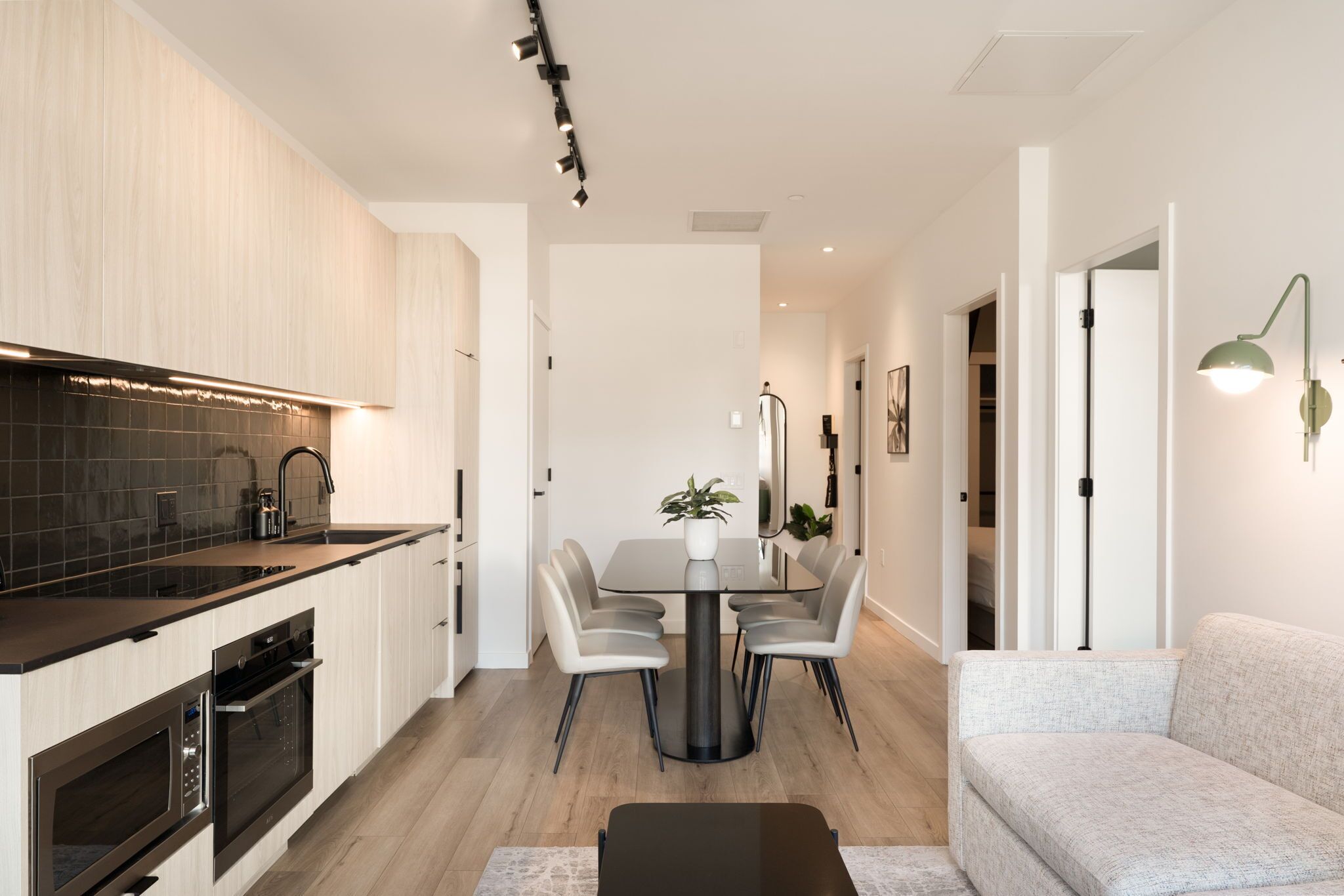 A modern kitchen with integrated appliances, a dining area with a round table and chairs, and a living space with a sofa and a lamp.