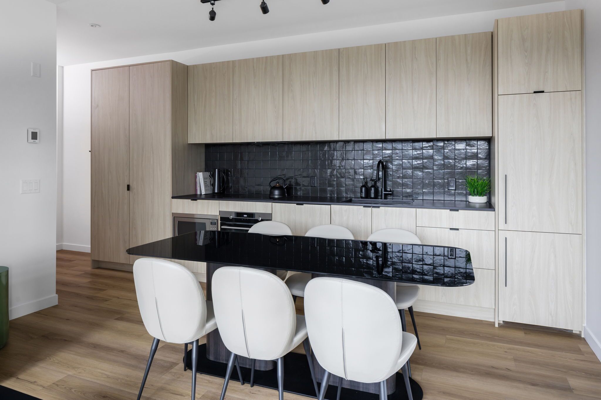 A modern kitchen with a black countertop, white chairs, and light wood cabinets.