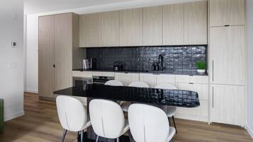 A modern kitchen with a black countertop, white chairs, and light wood cabinets.