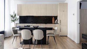 A modern kitchen with a central island, light wood cabinets, and a black backsplash. - Smithe House (Vancouver)
