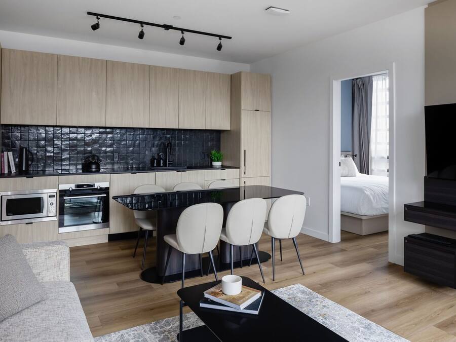A modern kitchen with built-in appliances, a dining area with chairs, and a living space with a sofa and a coffee table.