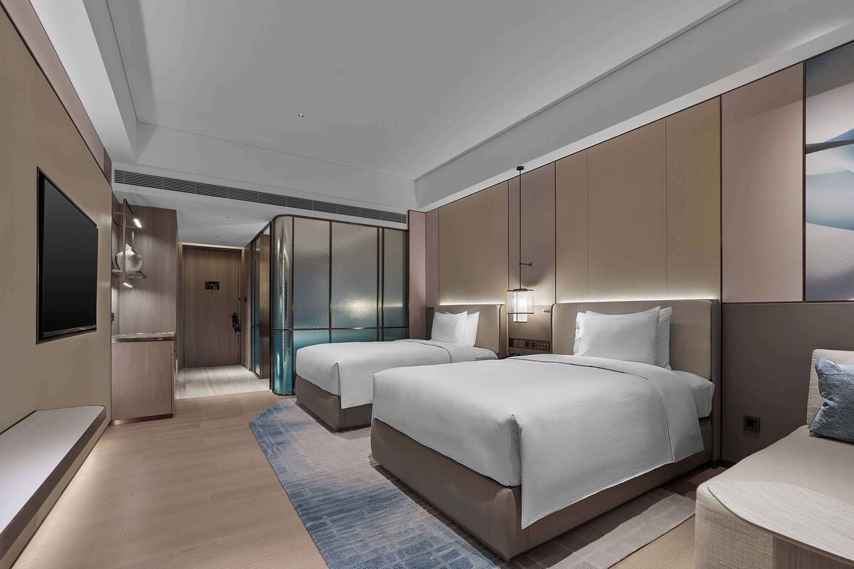 Quarto de hotel moderno com duas camas, um espelho grande e uma televisão.