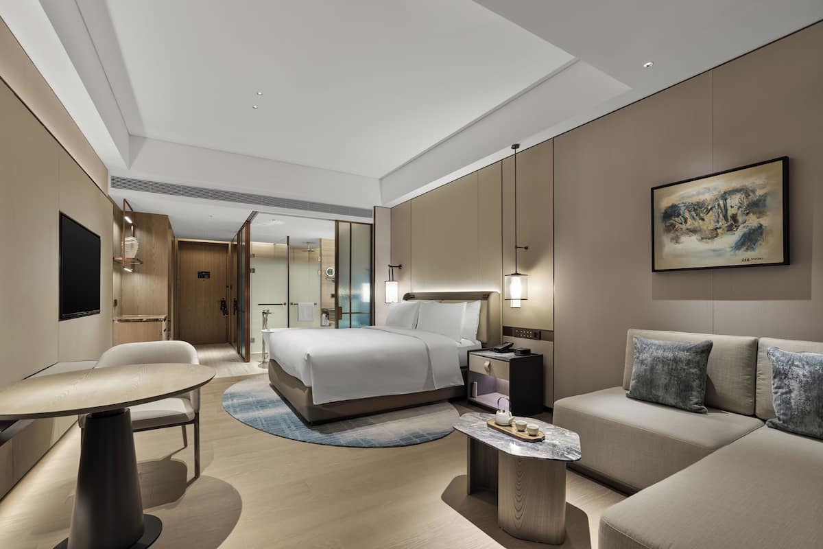 Quarto de hotel moderno com uma cama, um sofá, uma mesinha e um quadro na parede.
