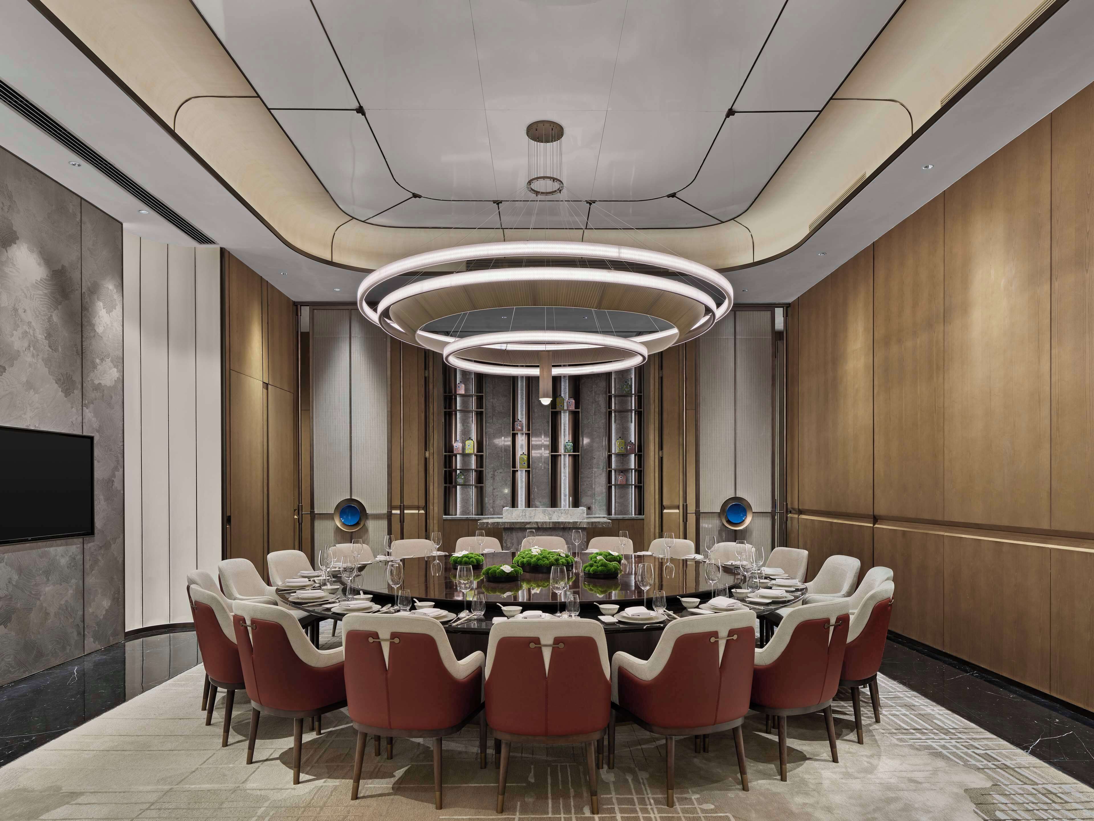 A modern conference room with a round table, red and white chairs, a large TV, and a unique ceiling design.