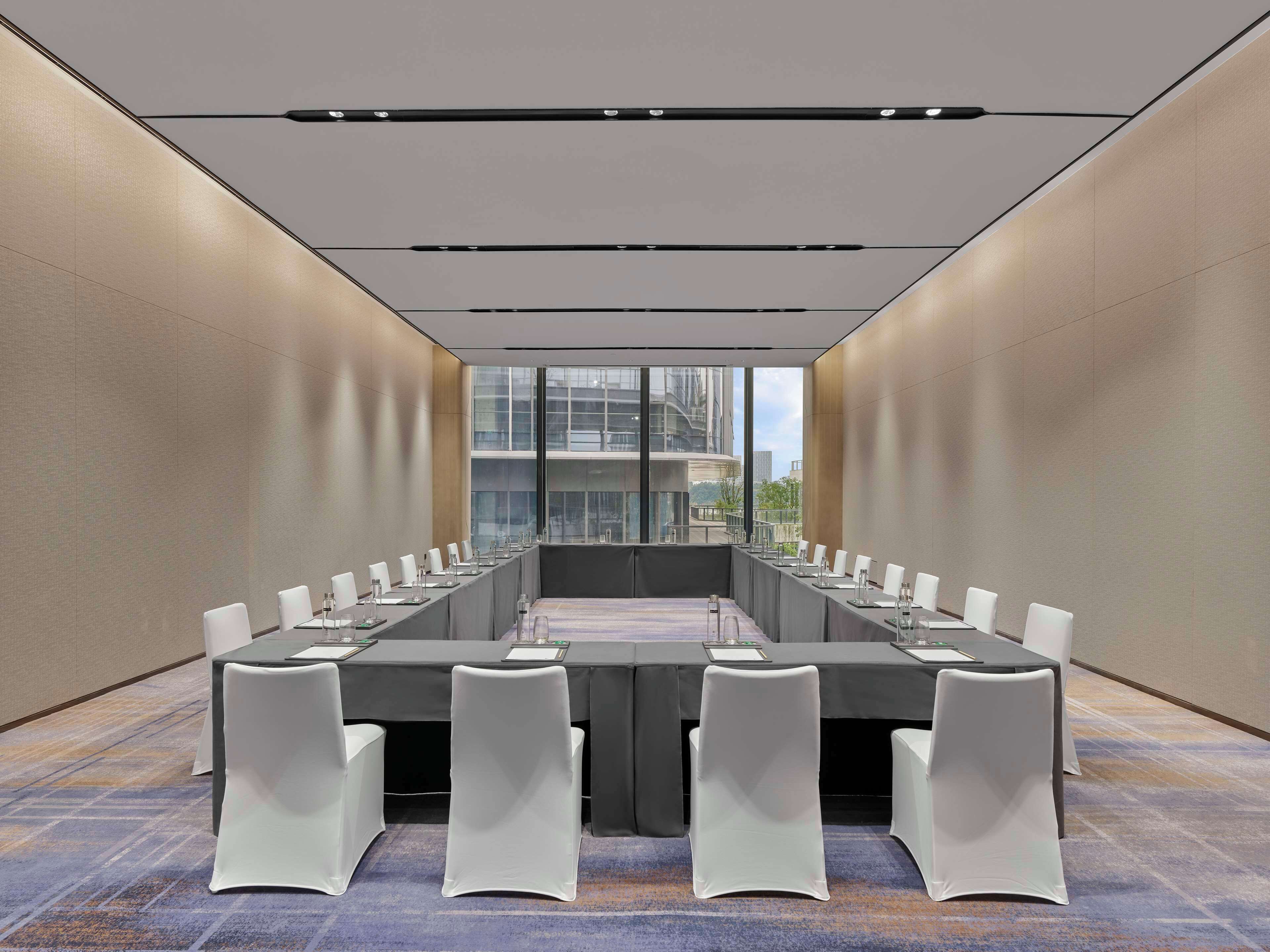A conference room with a long table, white chairs, and a city view through large windows.