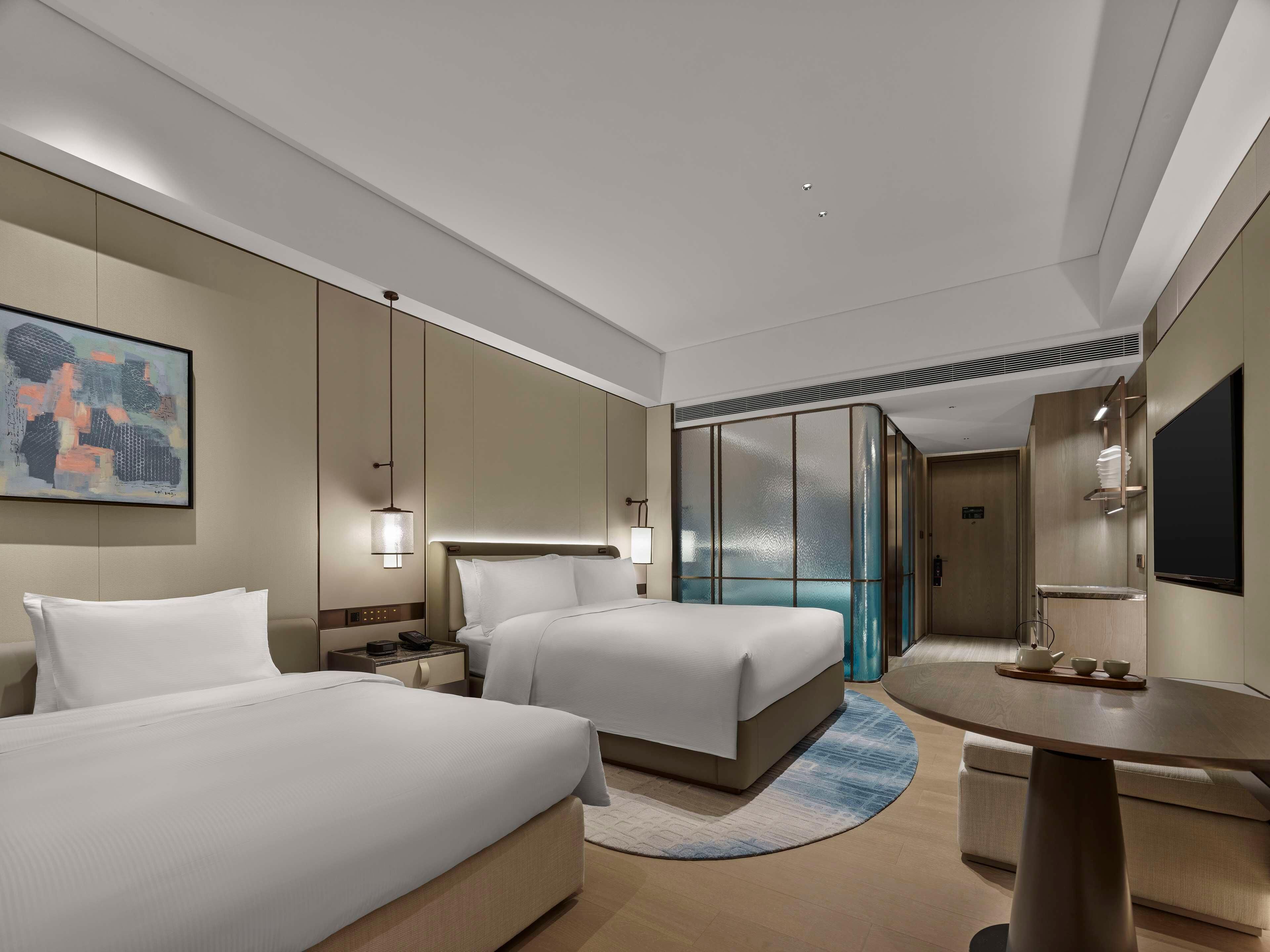 A hotel room with two beds, a desk, a TV, and a painting on the wall.