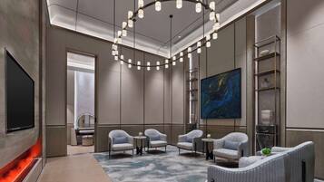 Eine moderne Hotellobby mit großem Flachbildfernseher, bequemen Sitzgelegenheiten, einer außergewöhnlichen Deckenleuchte und einem großen abstrakten Gemälde.