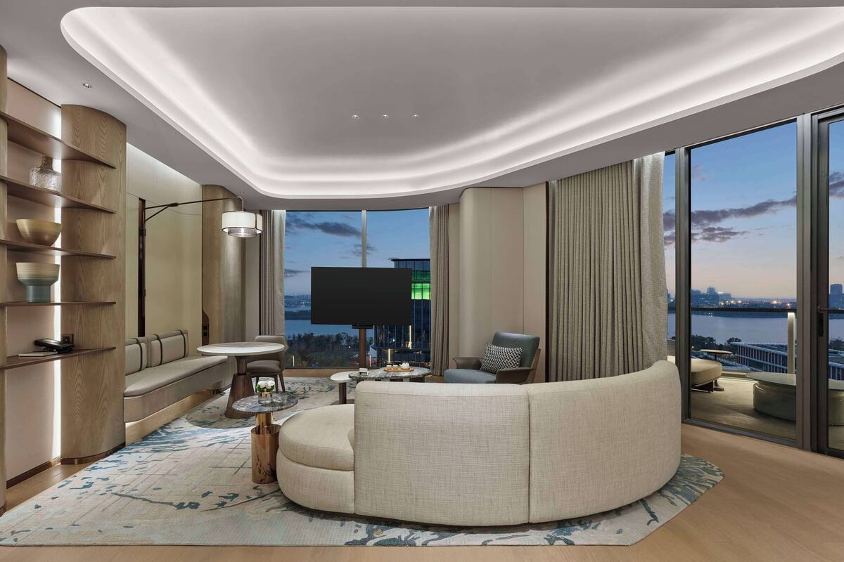 Uma sala de estar moderna com um sofá curvo, uma TV de tela plana e uma grande janela com vista para a cidade.