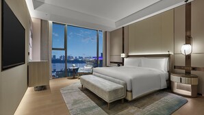 A modern hotel room with a large bed, a bedside table, a nightstand, a TV, and a view of the cityscape. - Doubletree By Hilton Chengdu Xinglong Lake (Chengdu)