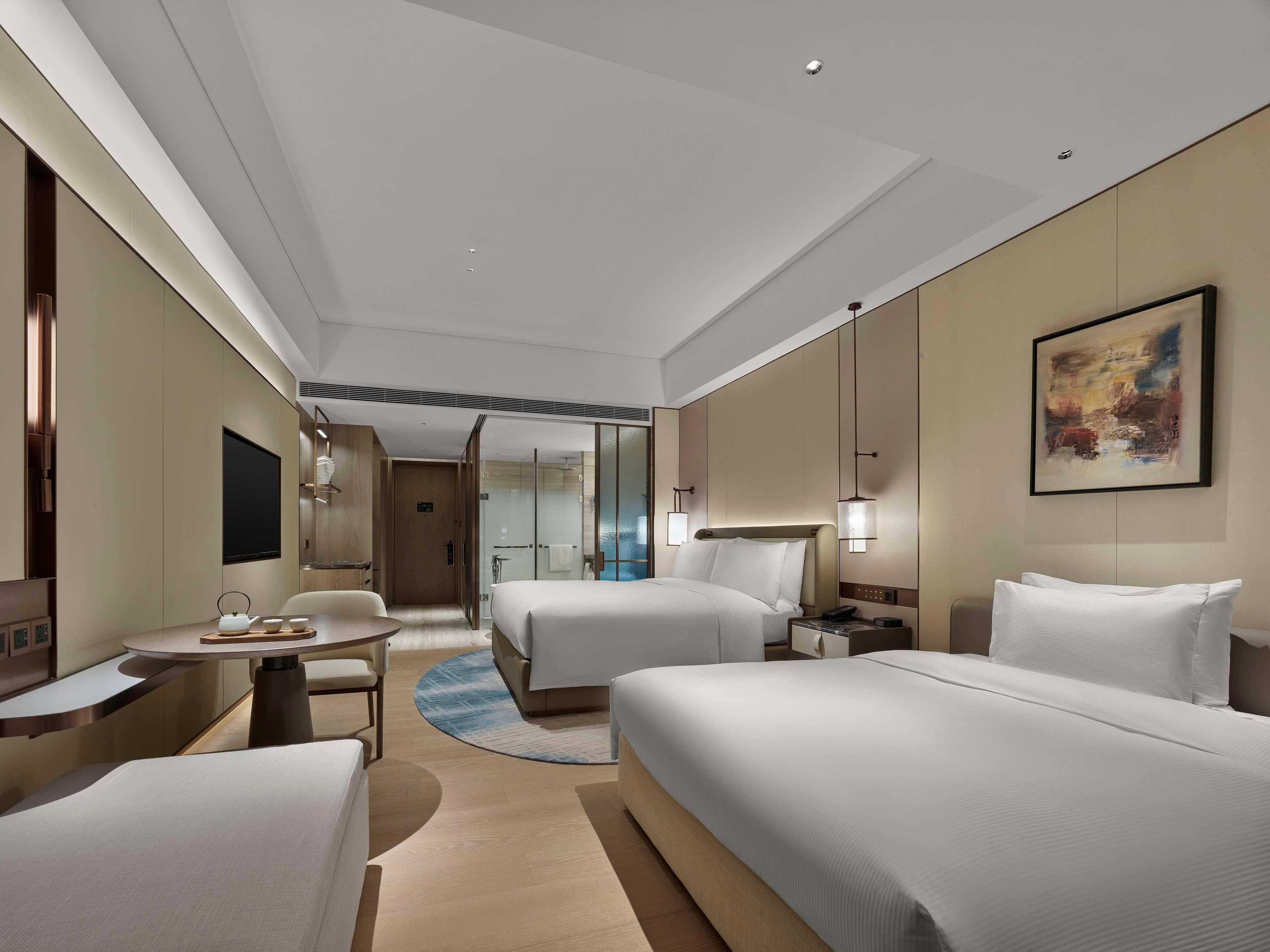 A hotel room with two beds, a desk, a chair, a TV, and a painting on the wall.