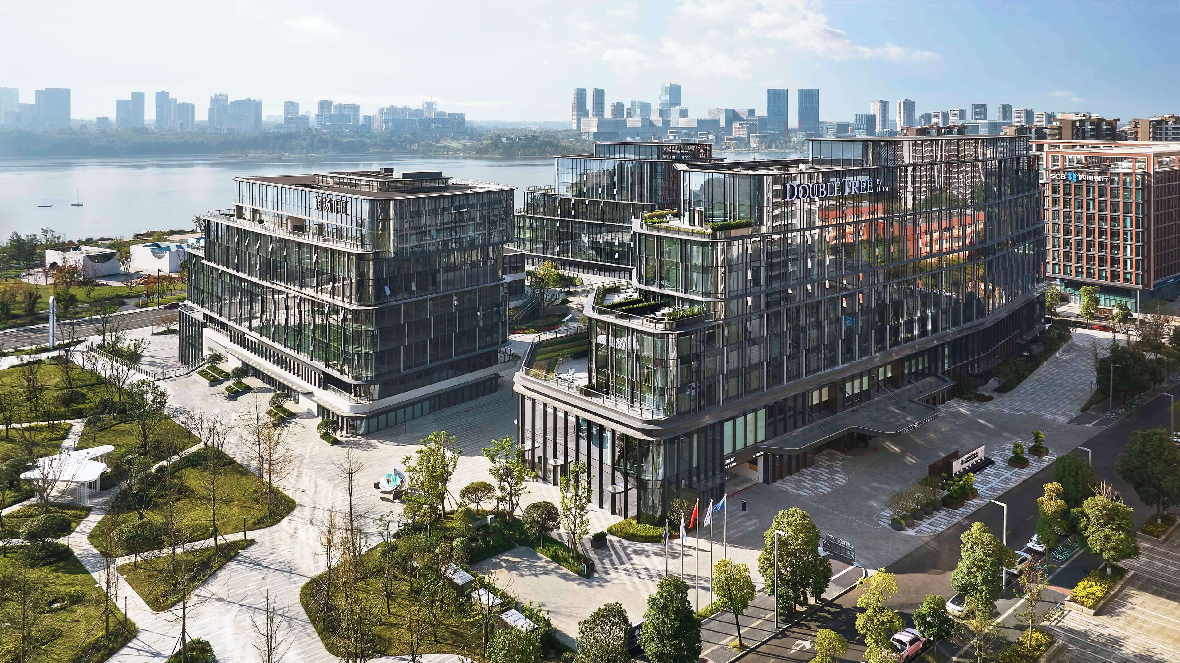 Et moderne hotel med en glasfacade, flere etager og udsigt til byens skyline.