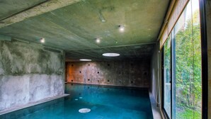Una piscina interior con techo de hormigón, un banco a lo largo de la pared y vistas a la vegetación exterior.
