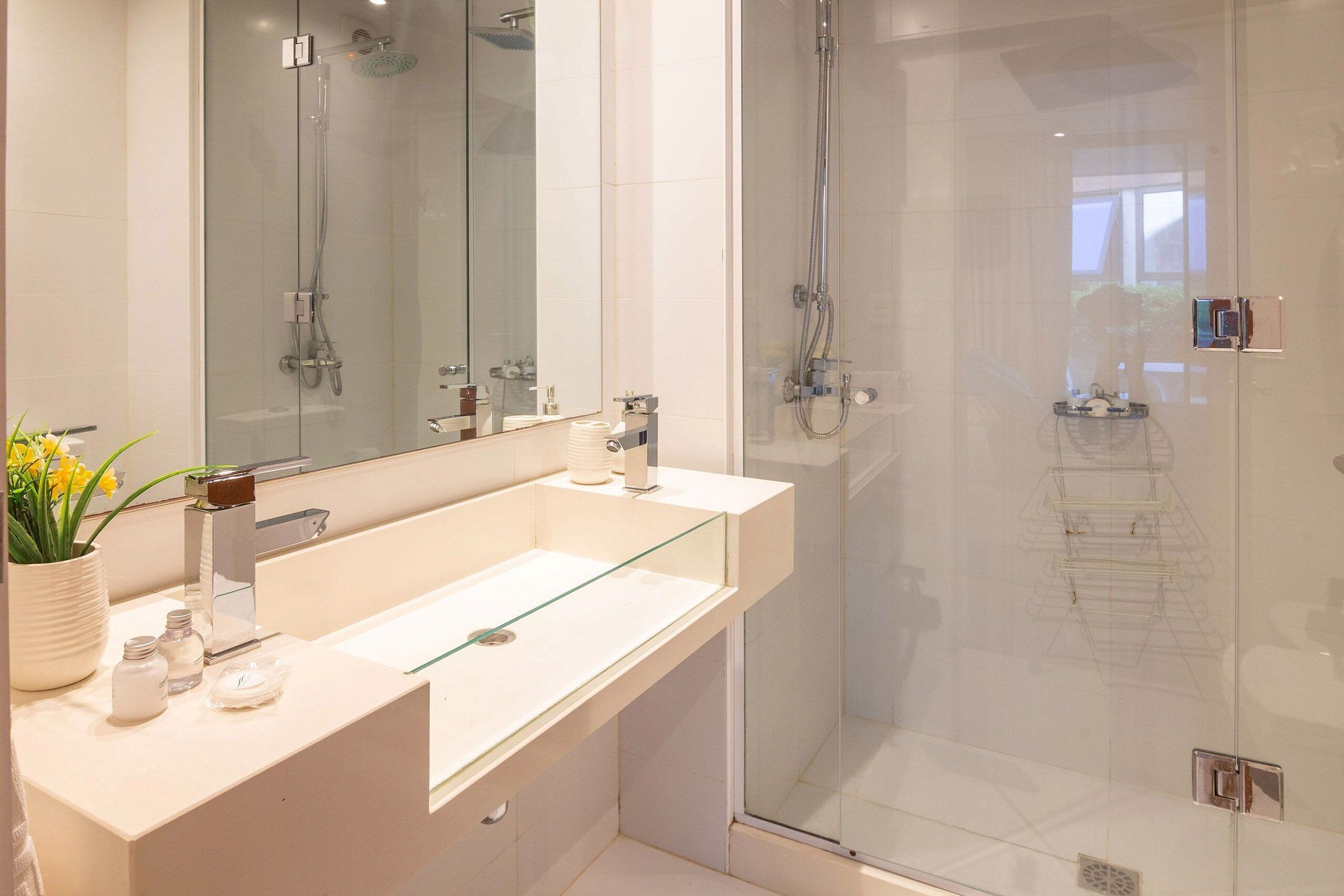 Un baño moderno con cabina de ducha de vidrio, un lavabo blanco y un espejo grande.