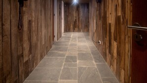 Un estrecho pasillo con paredes de madera y suelo de piedra, que conduce a una puerta con un picaporte de metal.