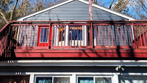 Una casa con un porche rojo y ventanas blancas, rodeada de árboles sin hojas bajo un cielo azul despejado.