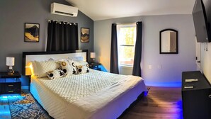 Un dormitorio con una cama, mesitas de noche, aire acondicionado, un espejo y una televisión.