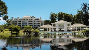 A hotel with a large building, a pool, and a reflection in the water. - Oceana Suites Green Park (Punta Ballena)