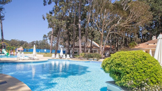 A swimming pool with lounge chairs, surrounded by trees and a building. - Oceana Suites Green Park (Punta Ballena)