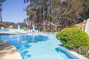 Piscina com espreguiçadeiras, cercada por árvores e um edifício.