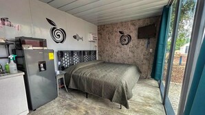 Ein kleines Zimmer mit Bett, Küchenzeile und Blick durch ein Fenster.
