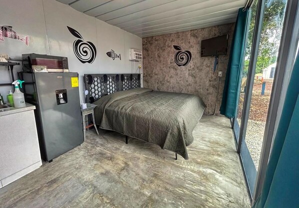 Habitación compacta con cama, kitchenette y vistas a través de una ventana.
