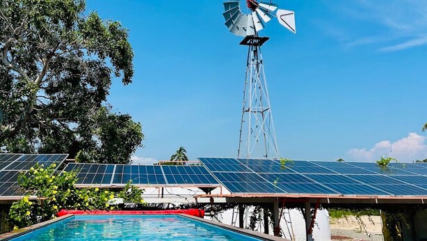 Ein Schwimmbecken mit Windmühle und Solaranlage im Hintergrund.
