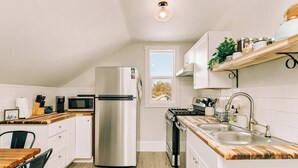 Una cocina moderna con armarios blancos, un refrigerador de acero inoxidable, un microondas, una estufa y una encimera de madera.